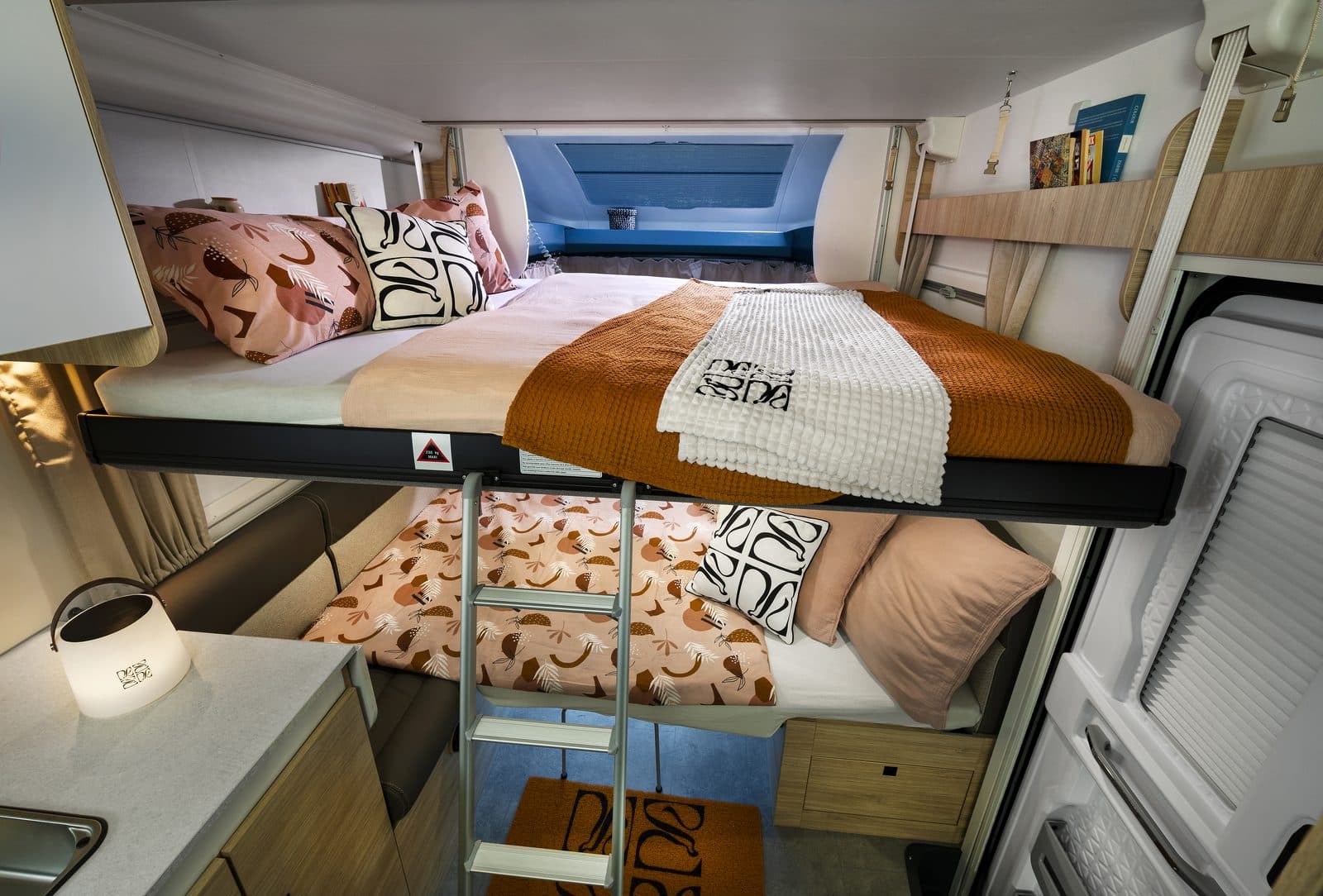 Intérieur du Chausson 640 : le lit de pavillon de 160 cm descendu au-dessus du salon, couette terracotta et coussins clairs, avec le couchage transformé du salon en dessous