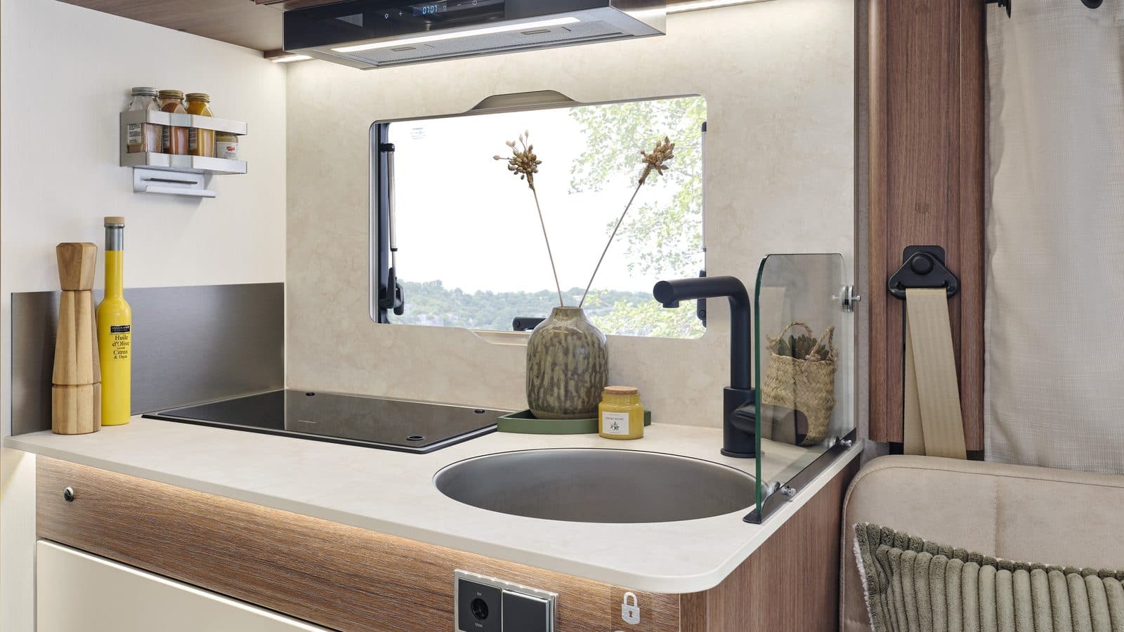 Cuisine du Fleurette Migrateur 69 LJG : plan de travail clair, évier rond, plaque de cuisson sous couvercle en verre, hotte aspirante, fenêtre et mobilier bois noyer
