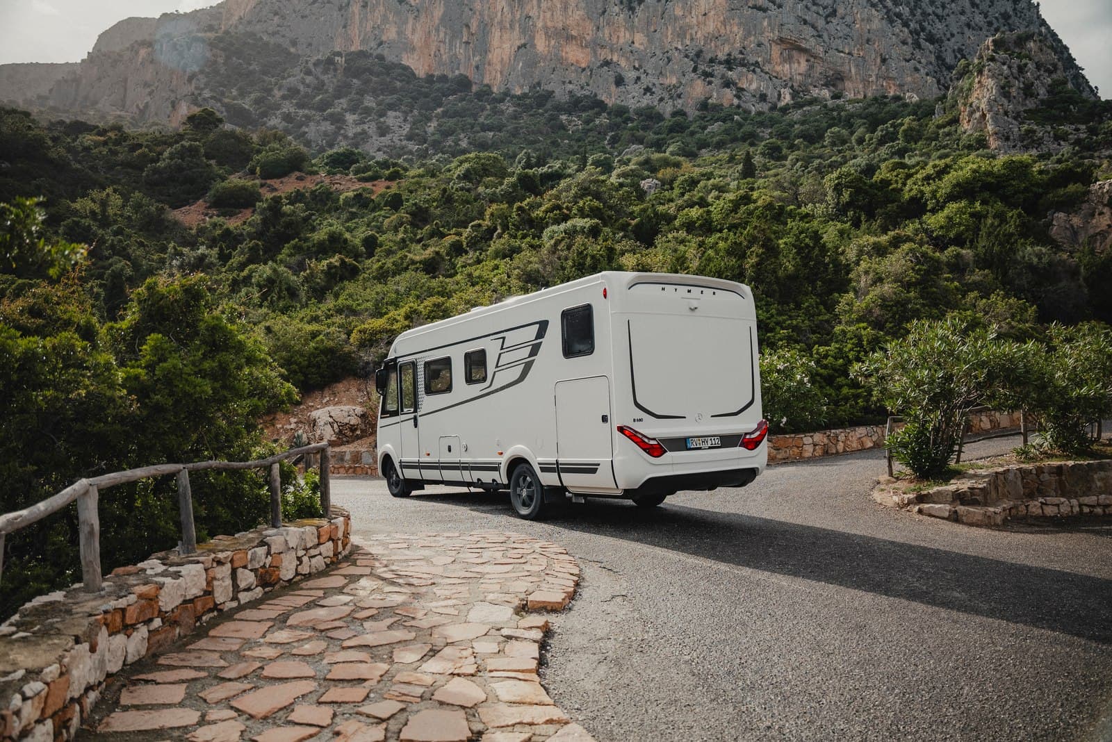 Intégral Hymer B-Klasse ModernComfort I 680 blanc vu de trois quarts arrière sur une route de montagne bordée de maquis, falaises calcaires en arrière-plan